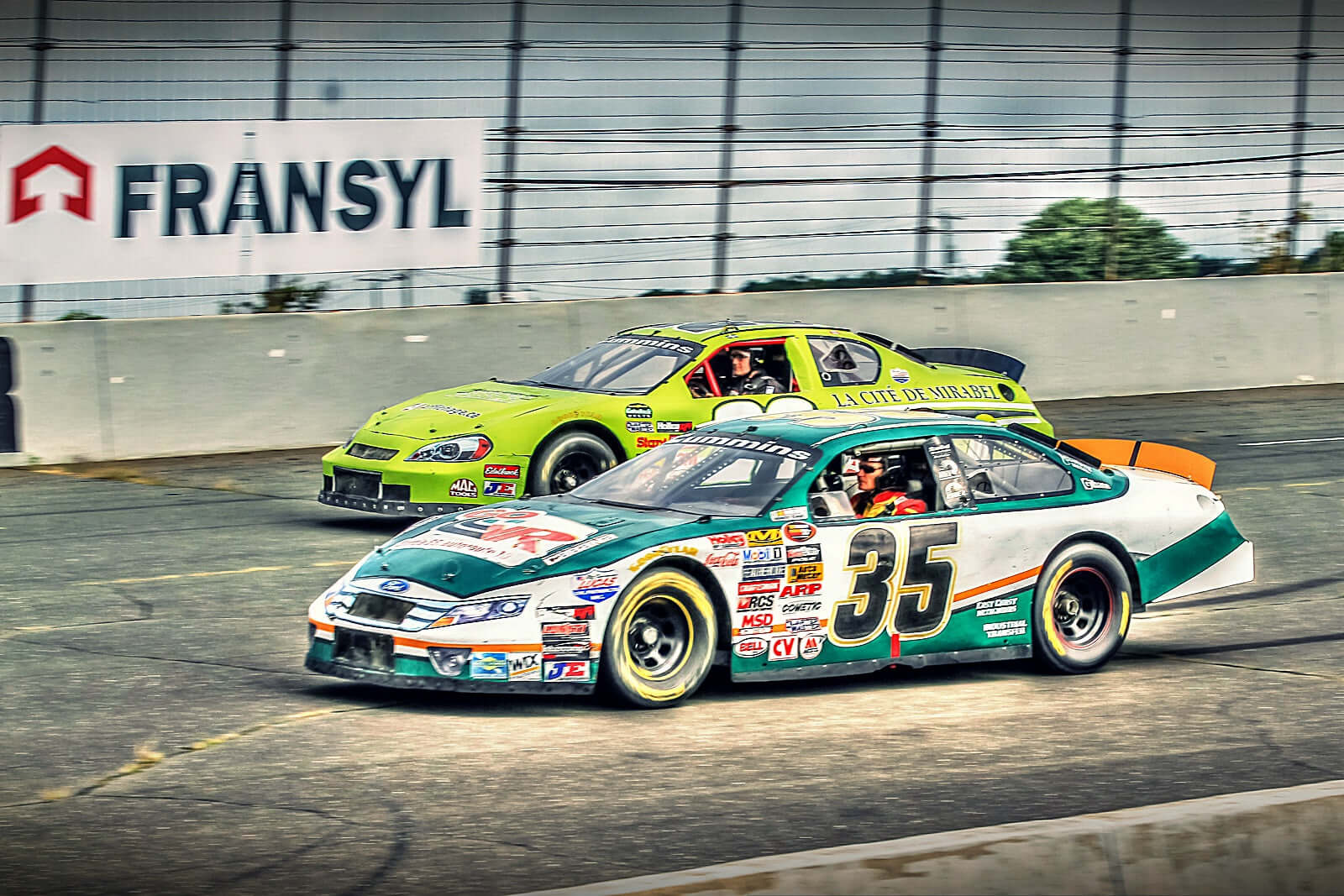 Deux voitures de course NASCAR en action sur le circuit, mettant en valeur la vitesse et la performance.